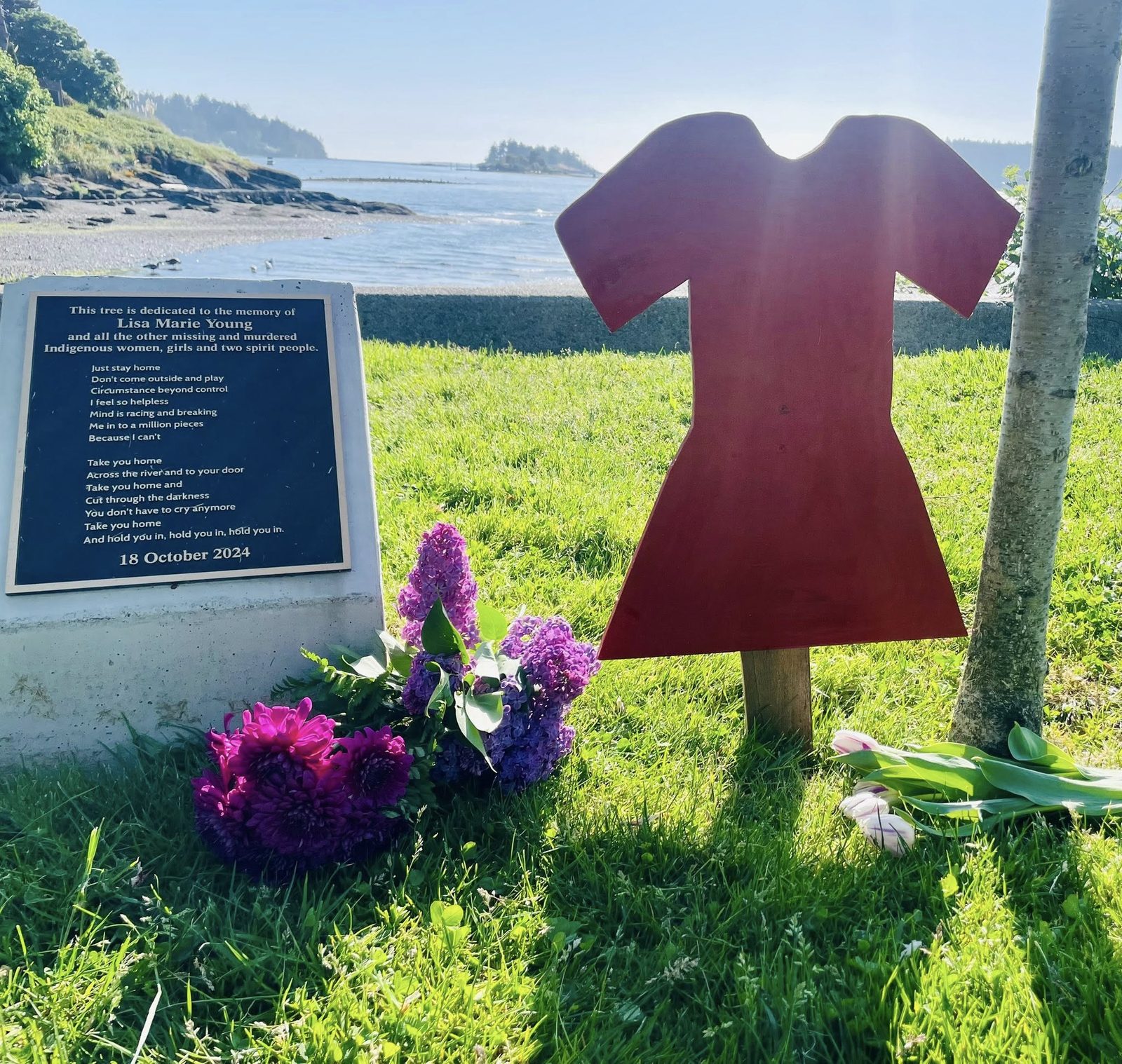 A cherry blossom tree dedicated to Lisa Marie Young, with a plaque and a red dress marker by the water